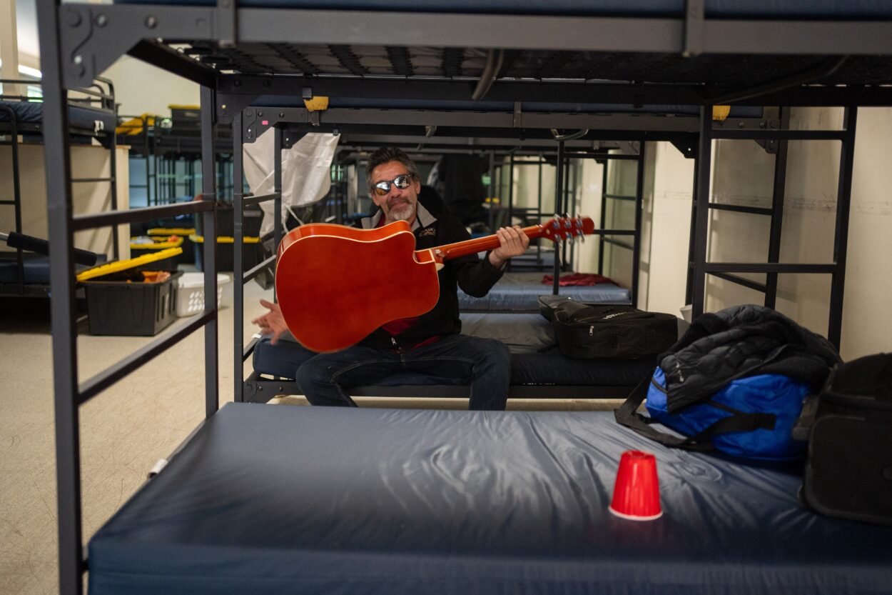 a man sitting on a bunk bed spins his guitar