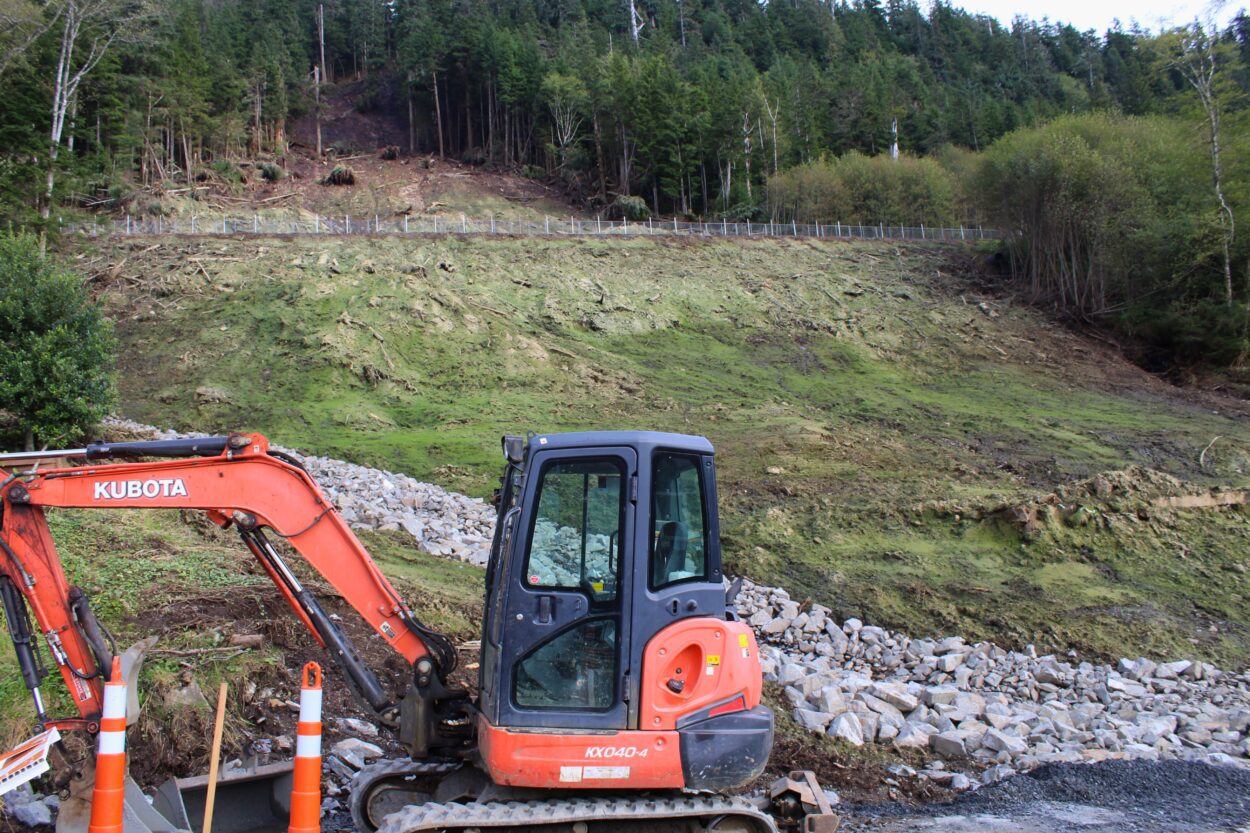 an open, treeless hillside covered in green hydroseeding with a construction vehicle in the foreground